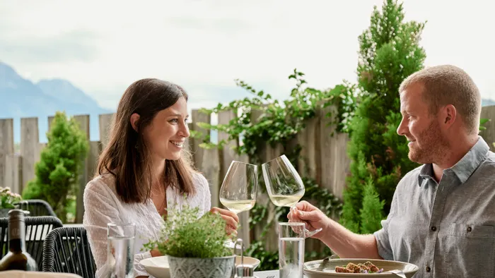 Paar stößt mit Weißwein im Außenrestaurant mit Bergblick an